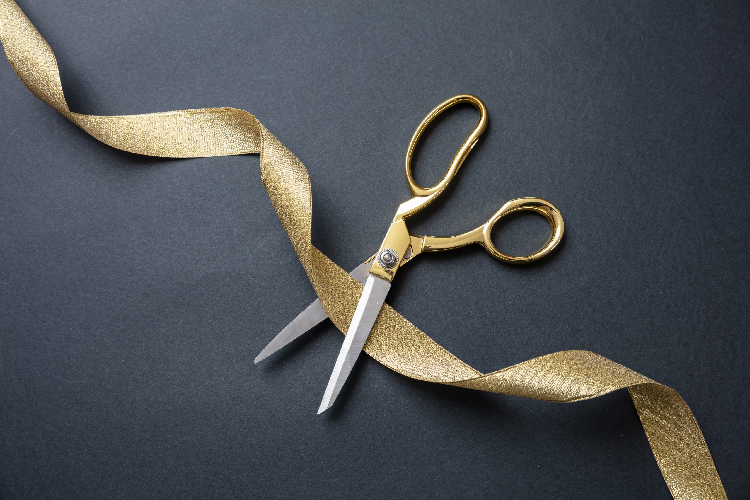 Grand opening. gold scissors cutting gold satin ribbon, black background